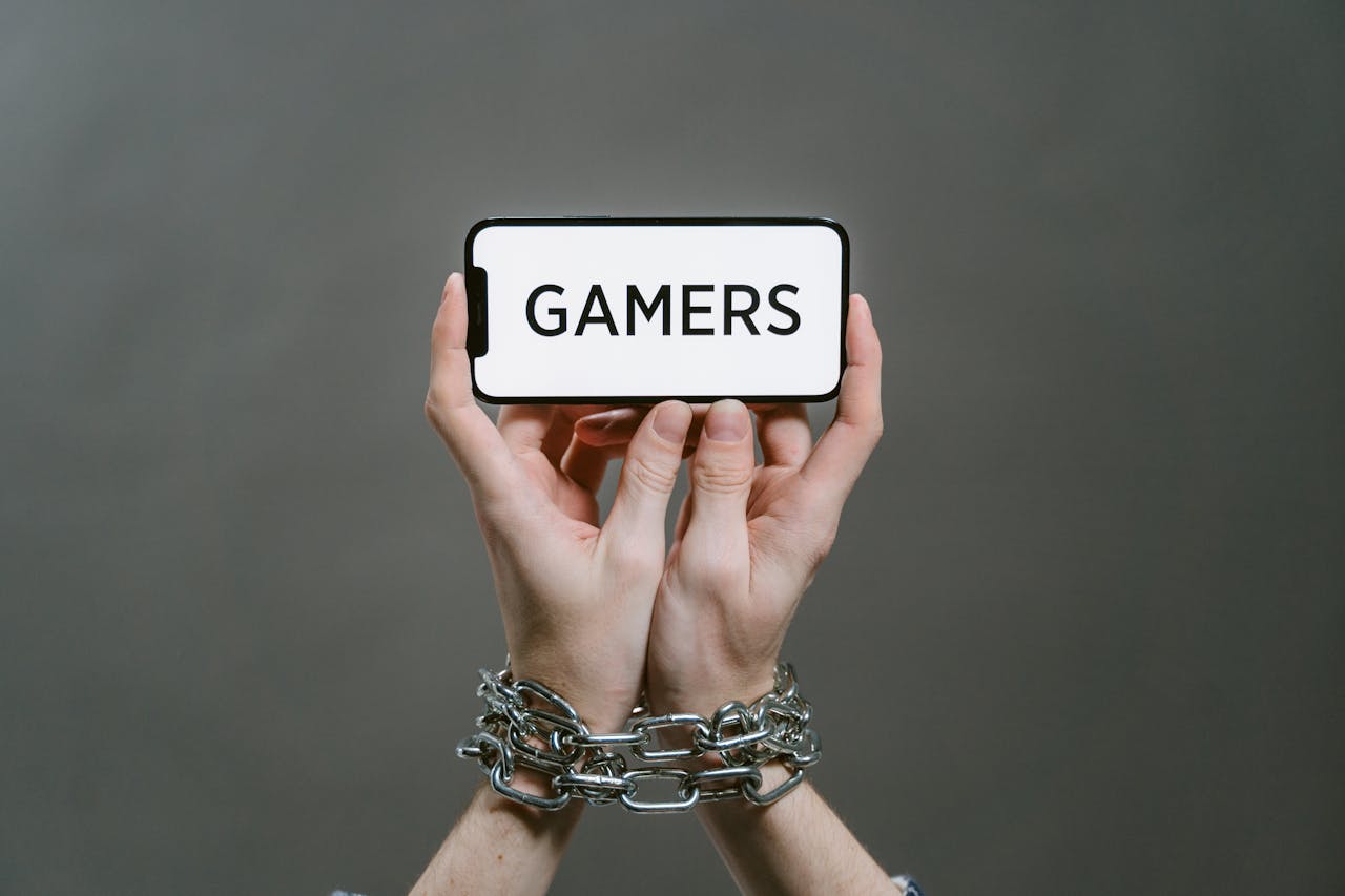 Conceptual image of a person holding a smartphone labeled GAMERS with chained hands.