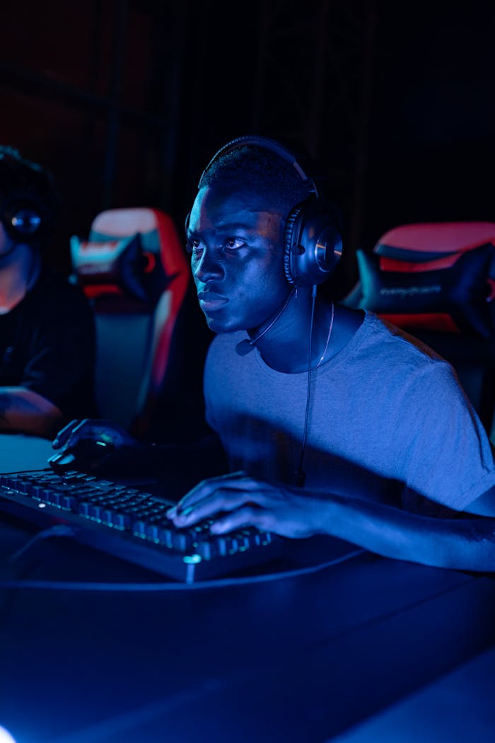 About A focused gamer wearing a headset at a computer gaming station at night.
